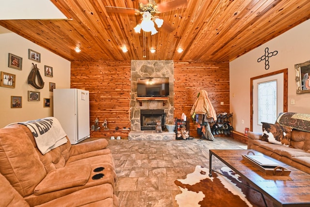 living room featuring ceiling fan, a stone fireplace, wooden ceiling, and wood walls