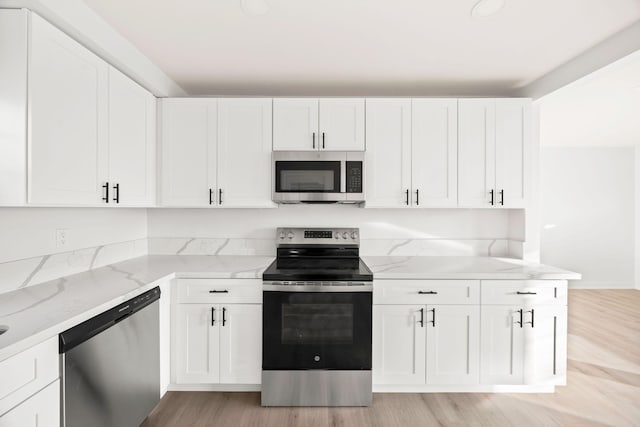 kitchen with white cabinets, light hardwood / wood-style floors, light stone counters, and stainless steel appliances