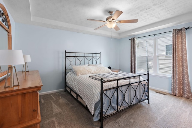 bedroom with dark colored carpet, ceiling fan, a textured ceiling, and a tray ceiling