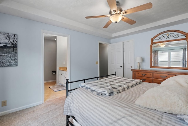 tiled bedroom with a raised ceiling, ensuite bath, and ceiling fan