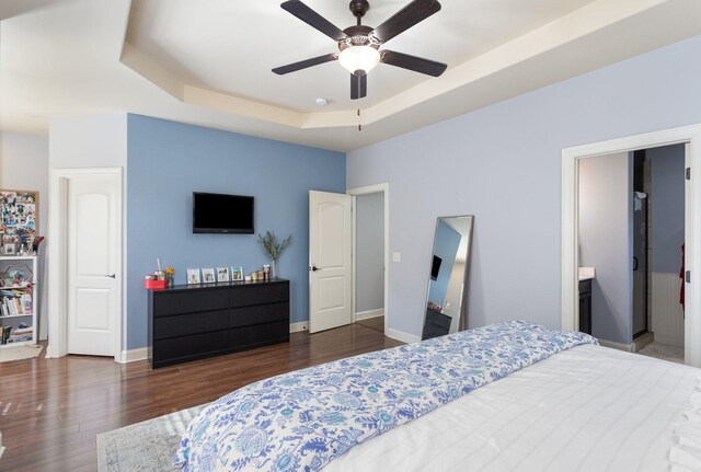 bedroom with ceiling fan, dark hardwood / wood-style flooring, ensuite bath, and a tray ceiling