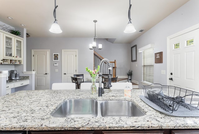 kitchen featuring light stone countertops, decorative light fixtures, an island with sink, and sink