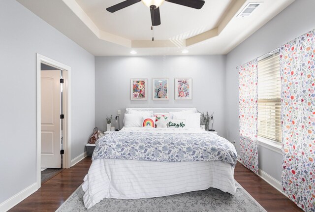 bedroom with dark hardwood / wood-style flooring, a tray ceiling, and ceiling fan