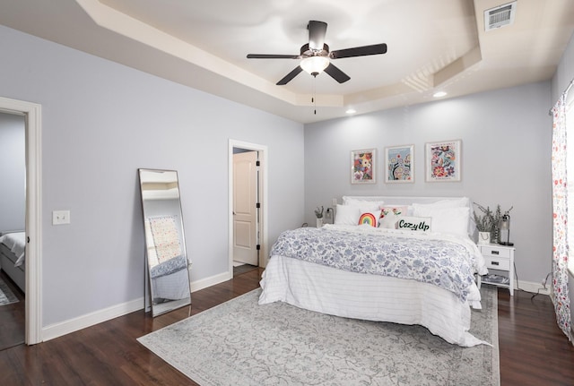 bedroom with a tray ceiling, ceiling fan, and dark wood-type flooring