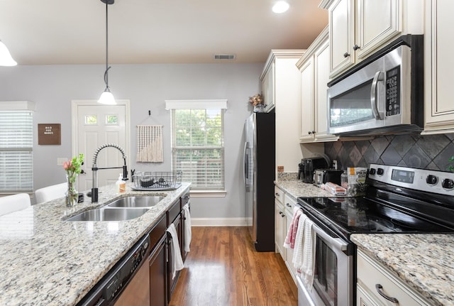 kitchen with sink, light stone counters, pendant lighting, decorative backsplash, and appliances with stainless steel finishes