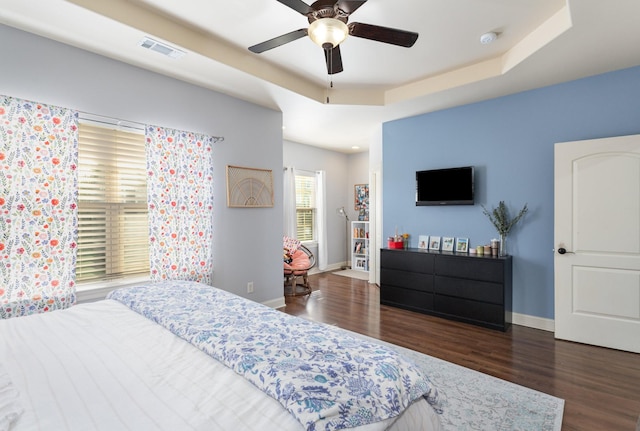 bedroom with ceiling fan, dark hardwood / wood-style floors, and a tray ceiling