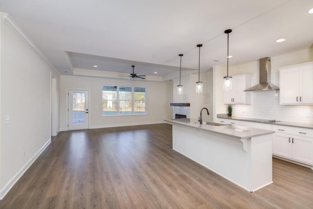 kitchen with white cabinets, an island with sink, wall chimney exhaust hood, and sink