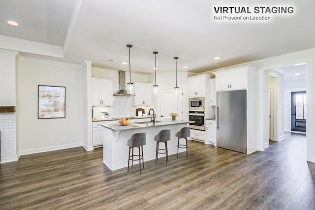 kitchen featuring wall chimney exhaust hood, a center island with sink, white cabinets, and appliances with stainless steel finishes