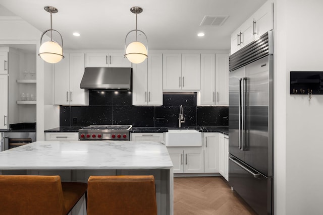 kitchen with pendant lighting, stove, white cabinetry, and built in refrigerator