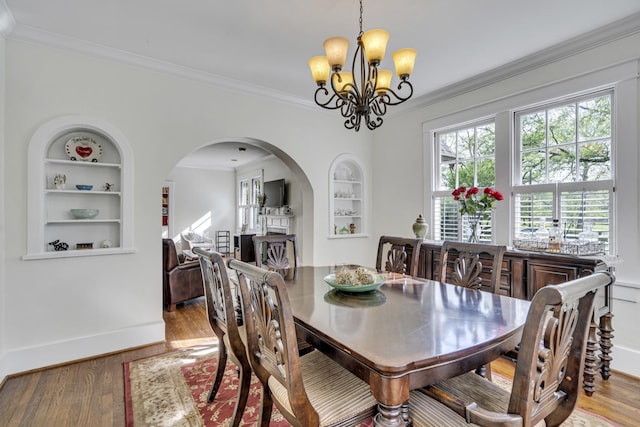 dining area featuring light wood-type flooring, built in features, ornamental molding, and an inviting chandelier