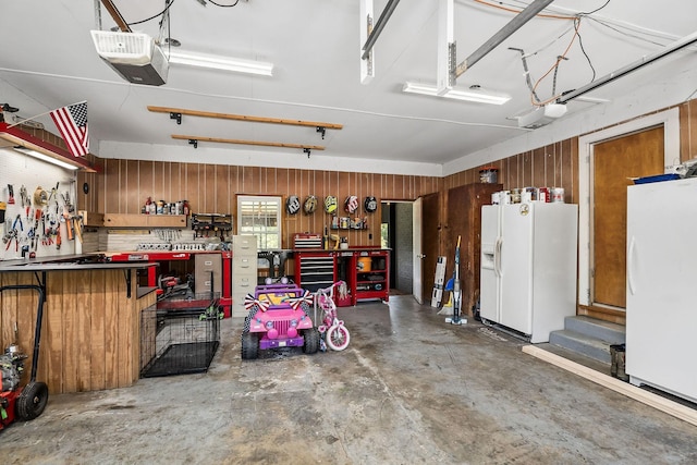 garage with a workshop area, white refrigerator with ice dispenser, white fridge, wooden walls, and a garage door opener