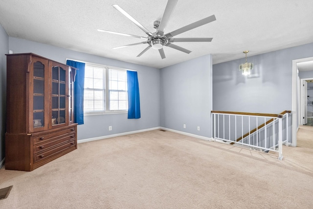 carpeted spare room featuring a textured ceiling, ceiling fan with notable chandelier, and baseboards