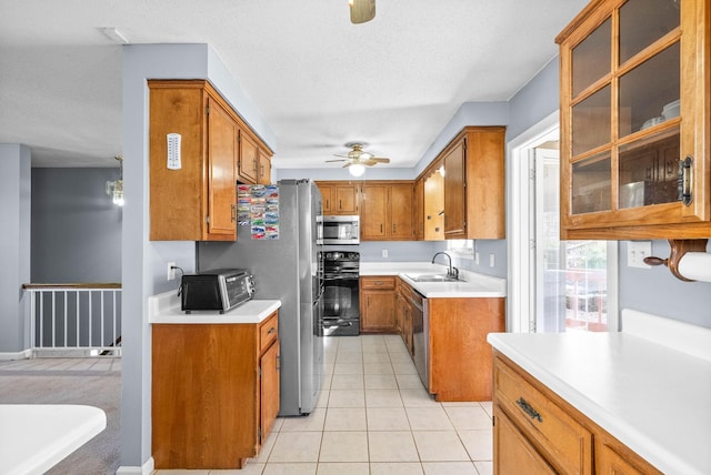 kitchen with brown cabinetry, ceiling fan, appliances with stainless steel finishes, a sink, and light tile patterned flooring