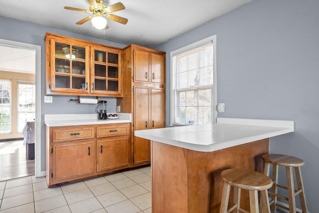 kitchen featuring brown cabinetry, light countertops, a peninsula, and a kitchen bar