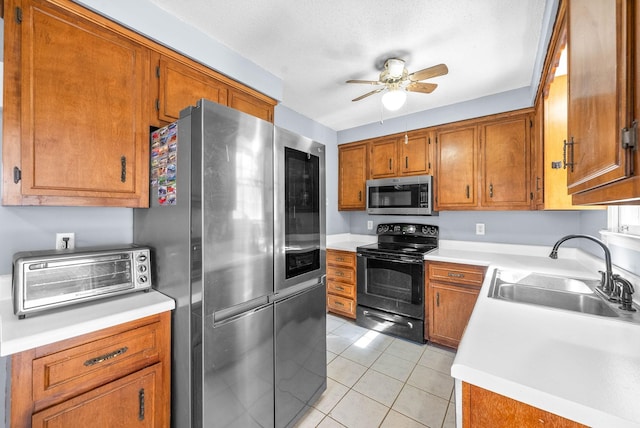 kitchen with light tile patterned floors, a toaster, brown cabinetry, appliances with stainless steel finishes, and a sink