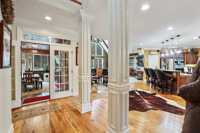 doorway featuring ornate columns, crown molding, and light wood-type flooring