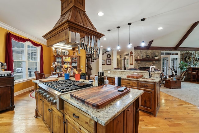 kitchen with a center island, light stone counters, light hardwood / wood-style floors, pendant lighting, and stainless steel gas stovetop