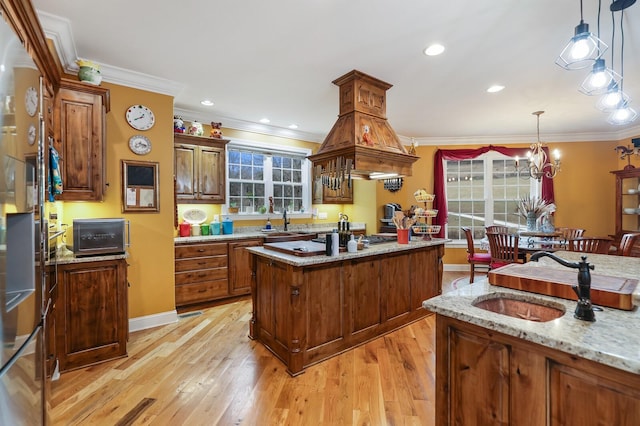 kitchen featuring sink, light stone counters, crown molding, pendant lighting, and a kitchen island