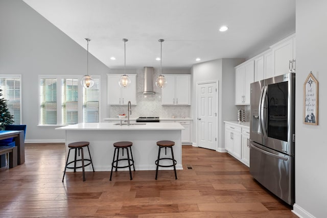 kitchen featuring white cabinets, appliances with stainless steel finishes, a kitchen island with sink, and wall chimney range hood