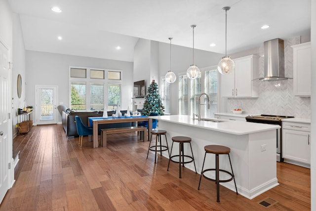 kitchen with backsplash, stainless steel range, sink, wall chimney range hood, and a center island with sink