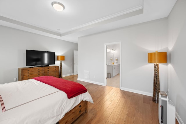 bedroom featuring a raised ceiling, connected bathroom, crown molding, and wood-type flooring