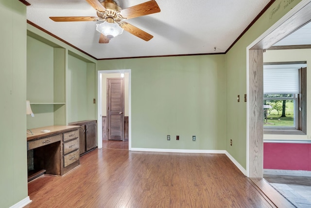 interior space featuring ceiling fan, built in desk, ornamental molding, a textured ceiling, and light hardwood / wood-style floors