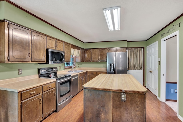 kitchen featuring sink, appliances with stainless steel finishes, crown molding, a kitchen island, and light wood-type flooring