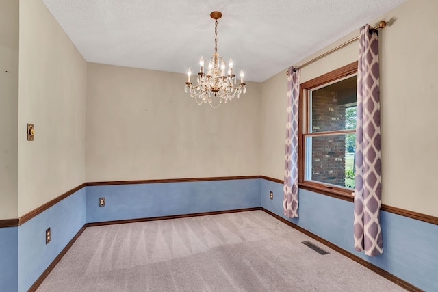 carpeted spare room featuring a textured ceiling and an inviting chandelier