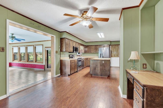 kitchen with appliances with stainless steel finishes, ornamental molding, a textured ceiling, wood-type flooring, and a center island