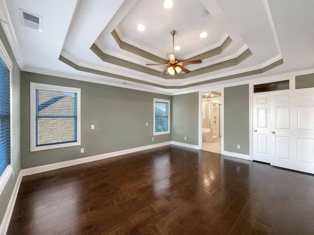 unfurnished bedroom with a tray ceiling, ensuite bath, dark wood-type flooring, and ornamental molding