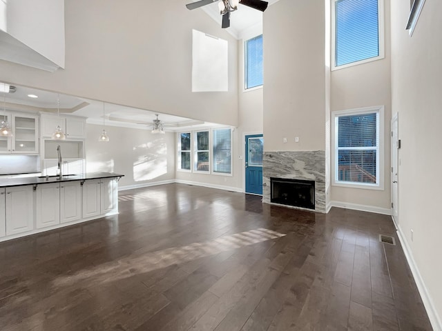 unfurnished living room with sink, a high end fireplace, a high ceiling, and dark hardwood / wood-style floors