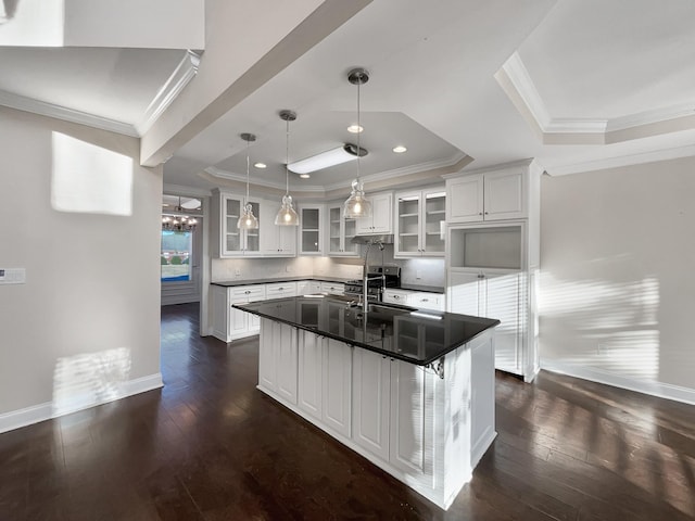 kitchen with a raised ceiling, white cabinetry, sink, and a kitchen island with sink