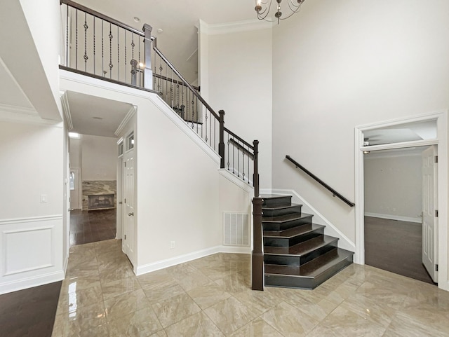 staircase with marble finish floor, ornamental molding, visible vents, a high ceiling, and a notable chandelier