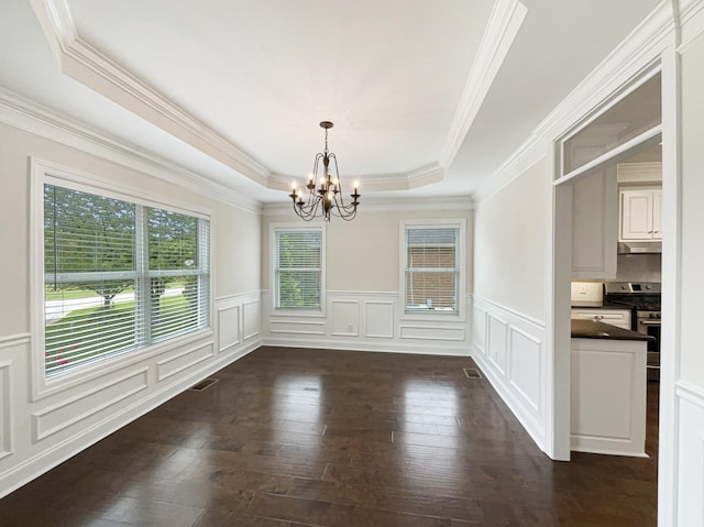 unfurnished dining area with a tray ceiling, ornamental molding, a chandelier, a decorative wall, and dark wood-type flooring