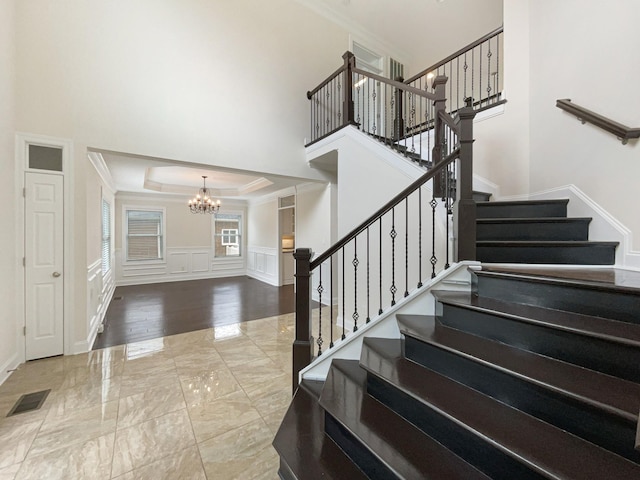 stairs featuring an inviting chandelier, visible vents, a decorative wall, marble finish floor, and ornamental molding