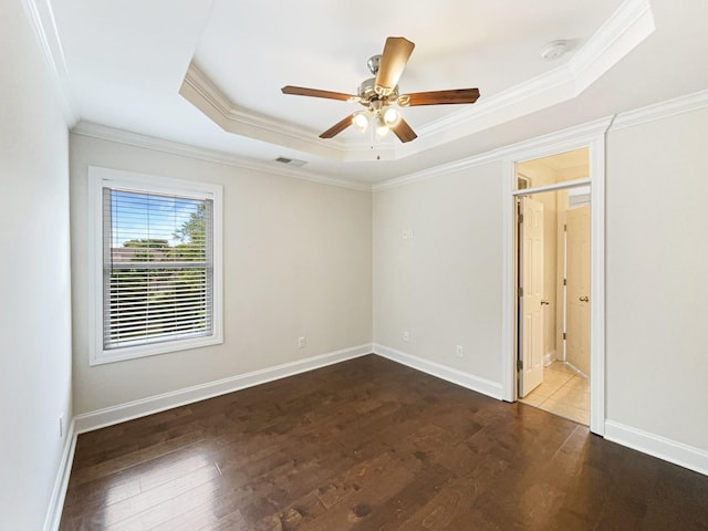 unfurnished bedroom featuring ornamental molding, visible vents, dark wood-style flooring, a raised ceiling, and baseboards