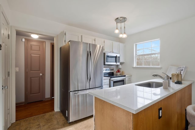 kitchen with appliances with stainless steel finishes, light stone counters, sink, decorative light fixtures, and white cabinetry