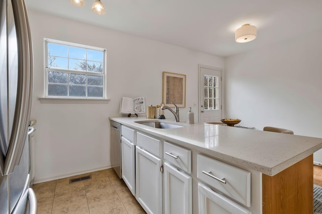 kitchen with dishwasher, sink, light tile patterned floors, kitchen peninsula, and white cabinets