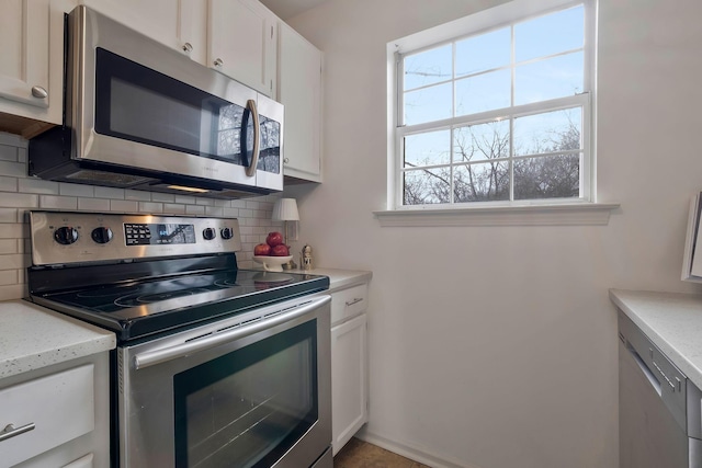 kitchen featuring white cabinets, appliances with stainless steel finishes, decorative backsplash, and light stone countertops