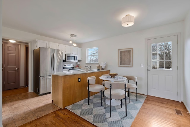 kitchen featuring kitchen peninsula, appliances with stainless steel finishes, sink, white cabinetry, and hanging light fixtures