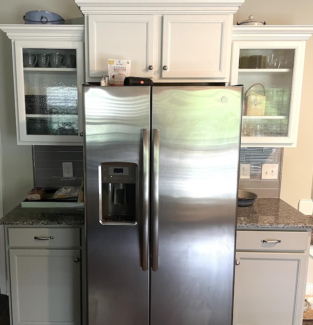 kitchen featuring stainless steel refrigerator with ice dispenser, backsplash, white cabinetry, and dark stone countertops