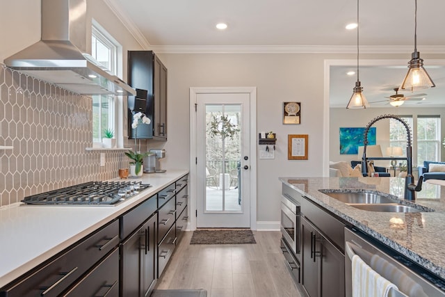 kitchen with sink, wall chimney range hood, dark brown cabinets, stainless steel appliances, and decorative light fixtures