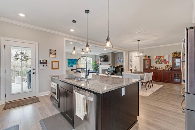 kitchen with sink, stainless steel appliances, light stone countertops, an island with sink, and decorative light fixtures