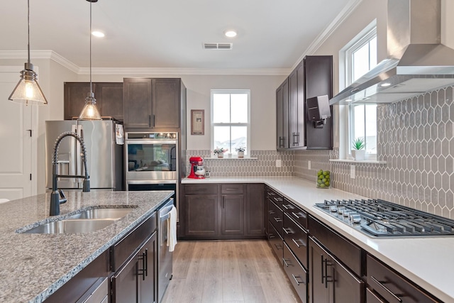 kitchen featuring wall chimney exhaust hood, sink, crown molding, stainless steel appliances, and decorative backsplash