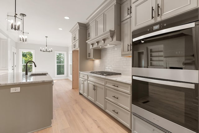 kitchen featuring stainless steel gas stovetop, hanging light fixtures, sink, an island with sink, and double oven