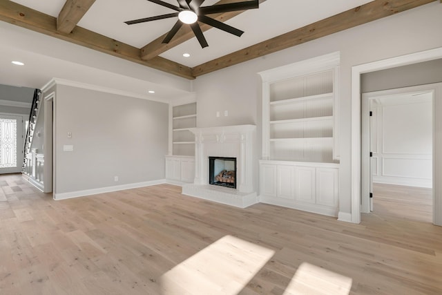 unfurnished living room featuring beam ceiling, built in shelves, ceiling fan, a brick fireplace, and light wood-type flooring