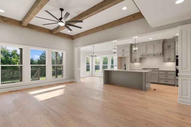 kitchen with gray cabinetry, beamed ceiling, an island with sink, decorative light fixtures, and decorative backsplash