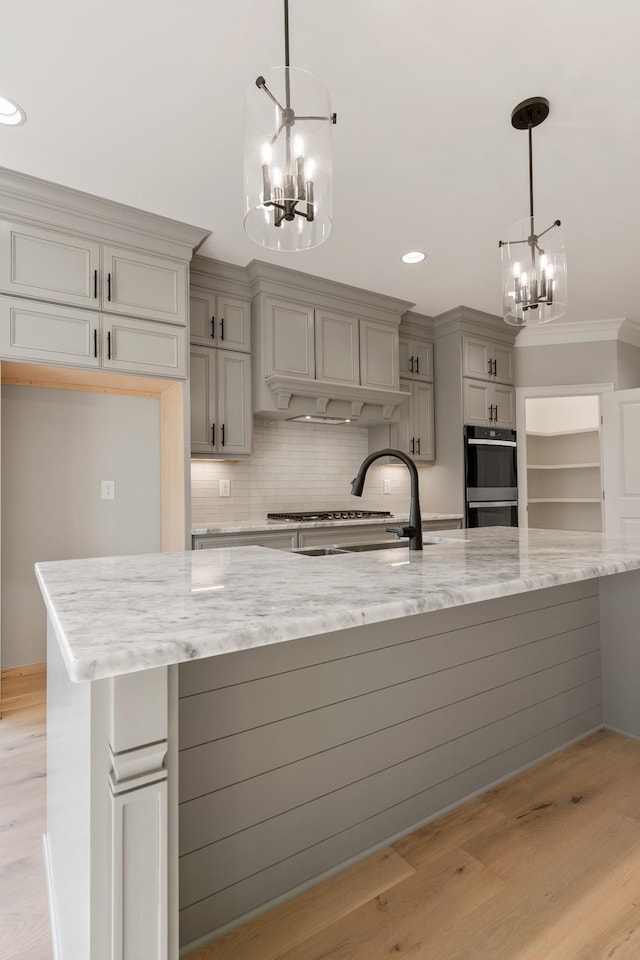 kitchen featuring pendant lighting, gray cabinetry, light stone countertops, double oven, and light hardwood / wood-style floors