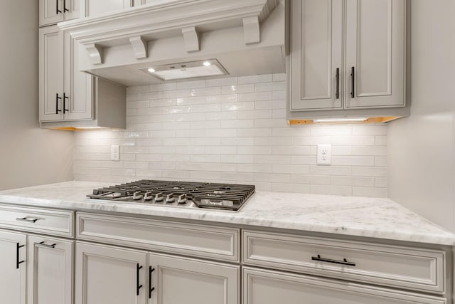 kitchen featuring premium range hood, decorative backsplash, light stone countertops, and stainless steel gas cooktop