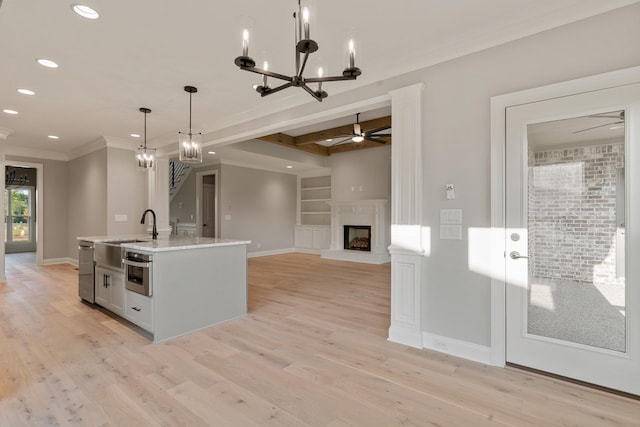 kitchen with built in shelves, ceiling fan with notable chandelier, a kitchen island with sink, decorative light fixtures, and oven